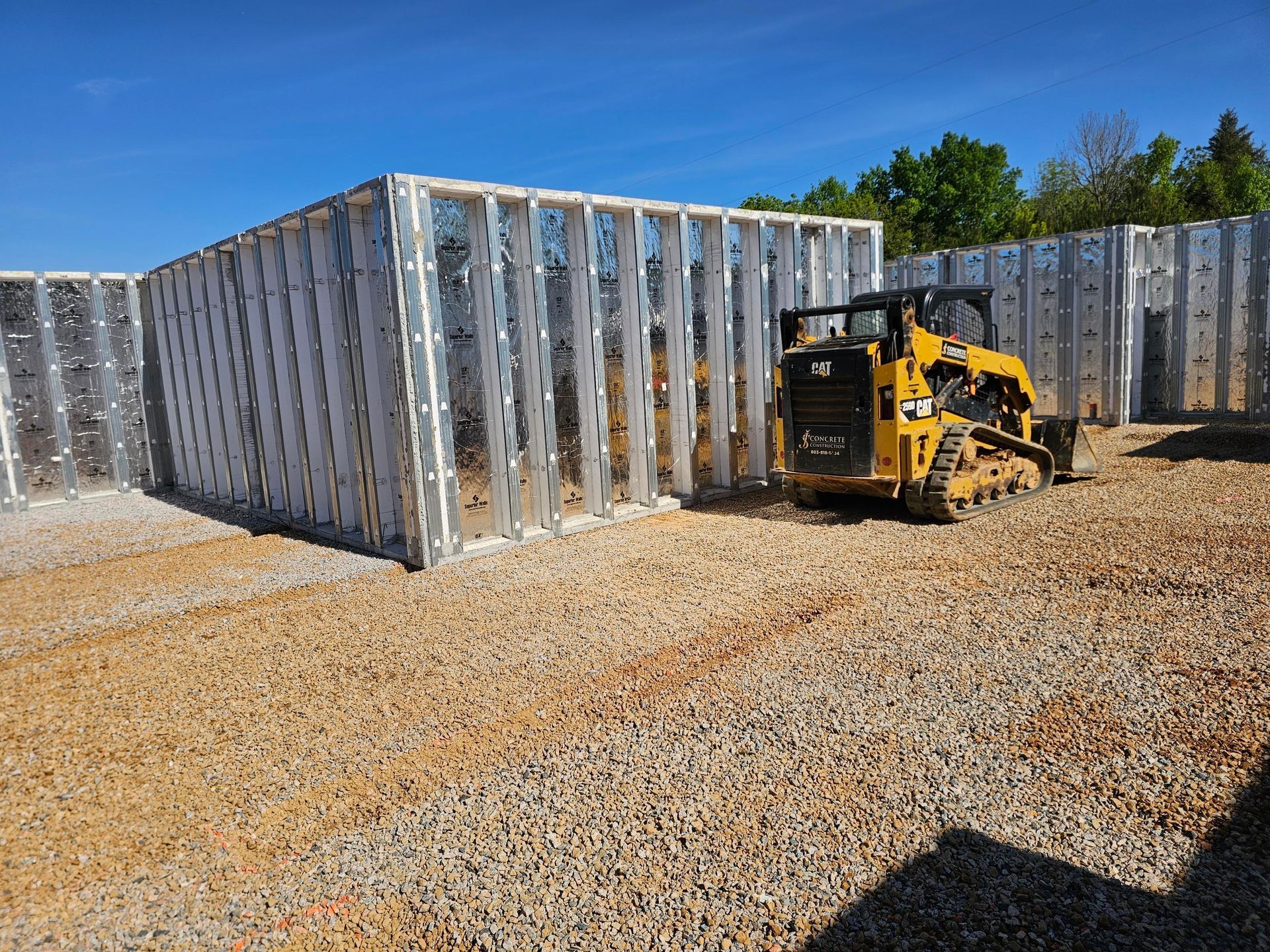 Yellow skid steer operating inside a gravel-filled foundation with metal walls against a blue sky.