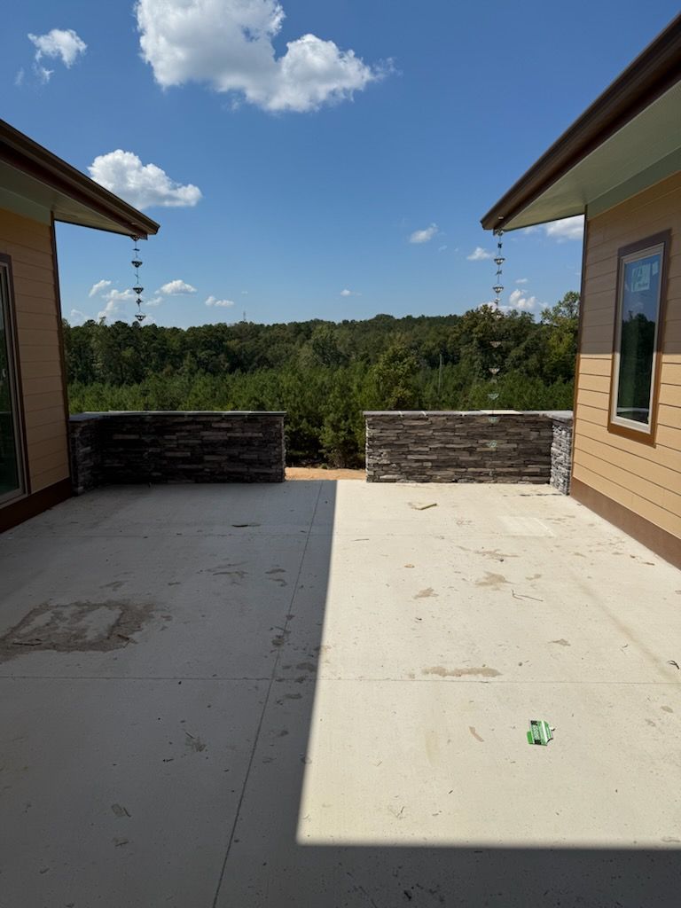 Two buildings with stone walls on a concrete patio overlooking trees and a blue sky.