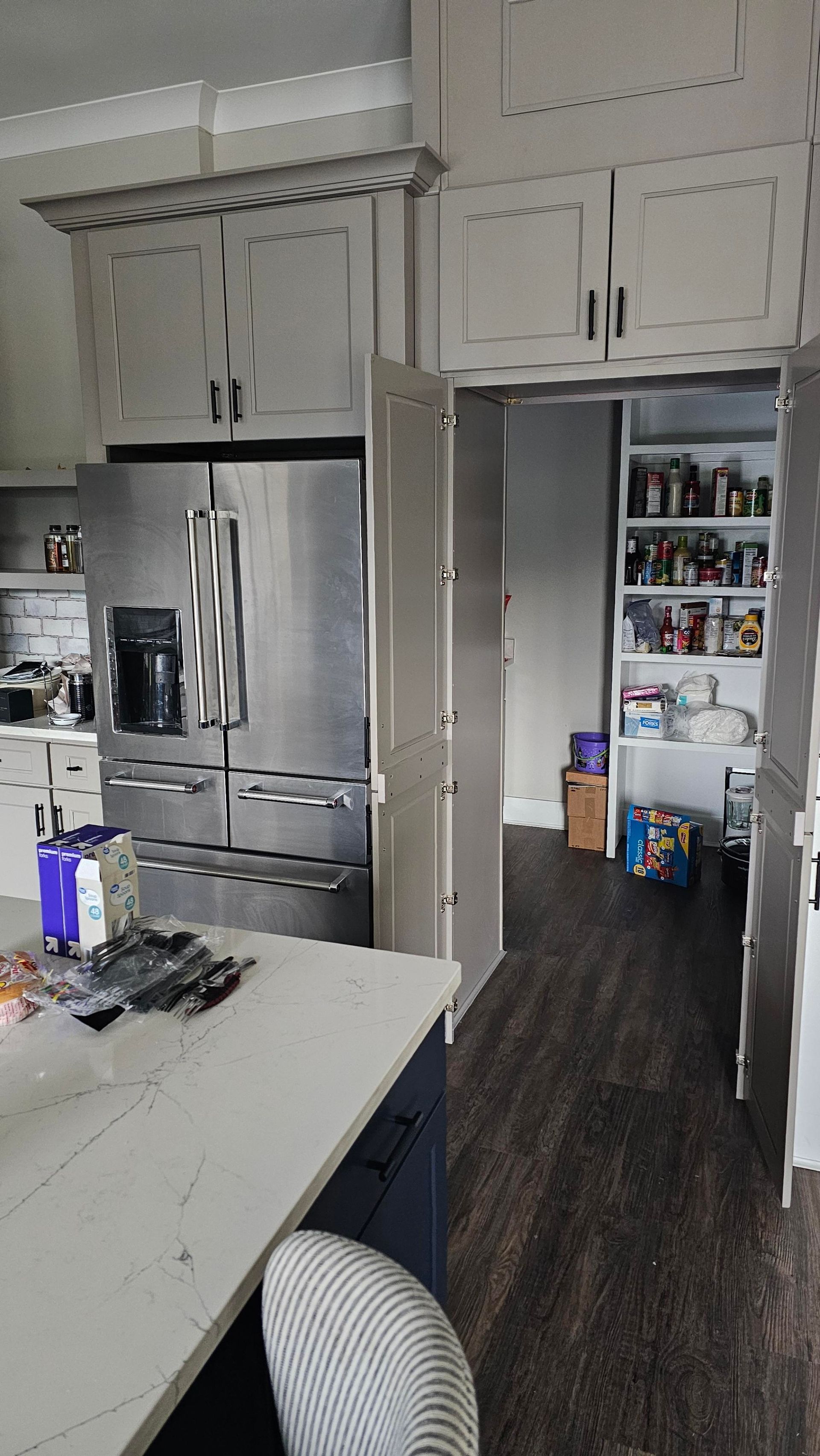 Kitchen with stainless steel refrigerator, pantry, and white cabinetry. Dark flooring, blue island.