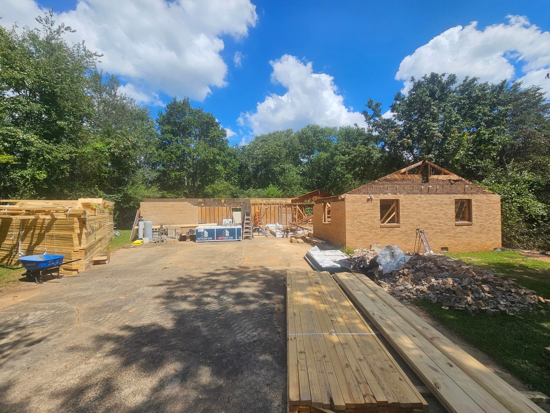 Construction site with unfinished earthen-toned brick building, wooden framing, lumber, and blue sky.