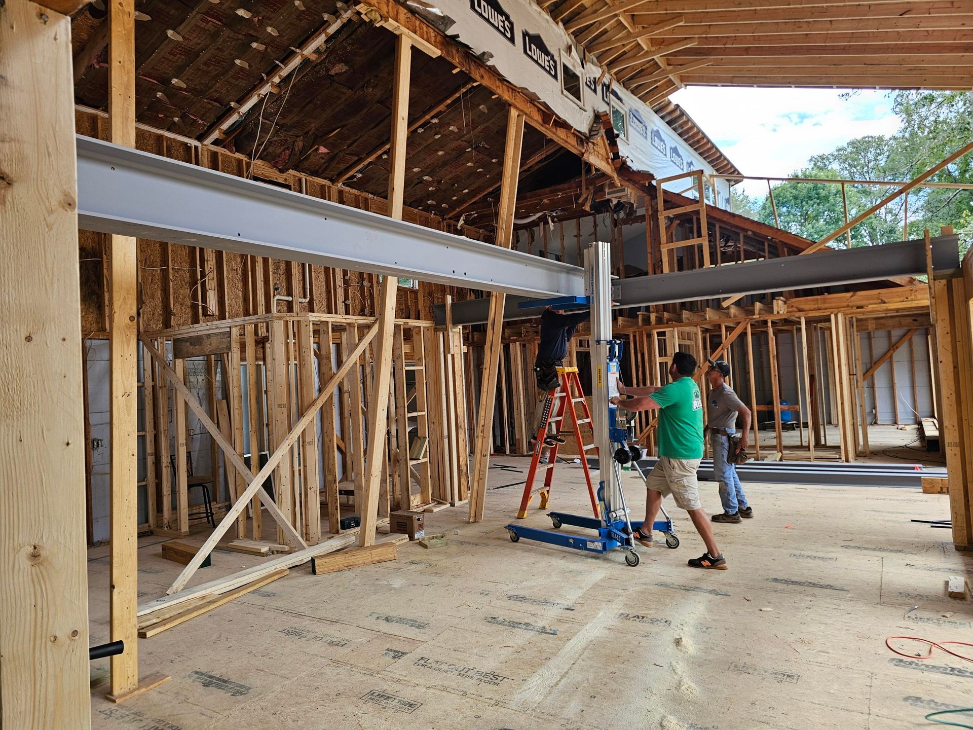Construction workers using a lift to install a steel beam inside a wooden framed building.