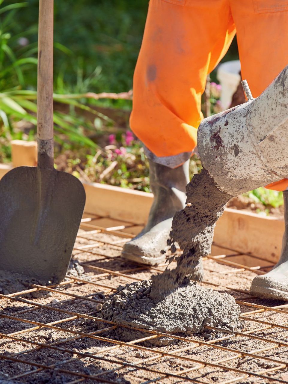 A person is pouring concrete into a grid with a shovel.