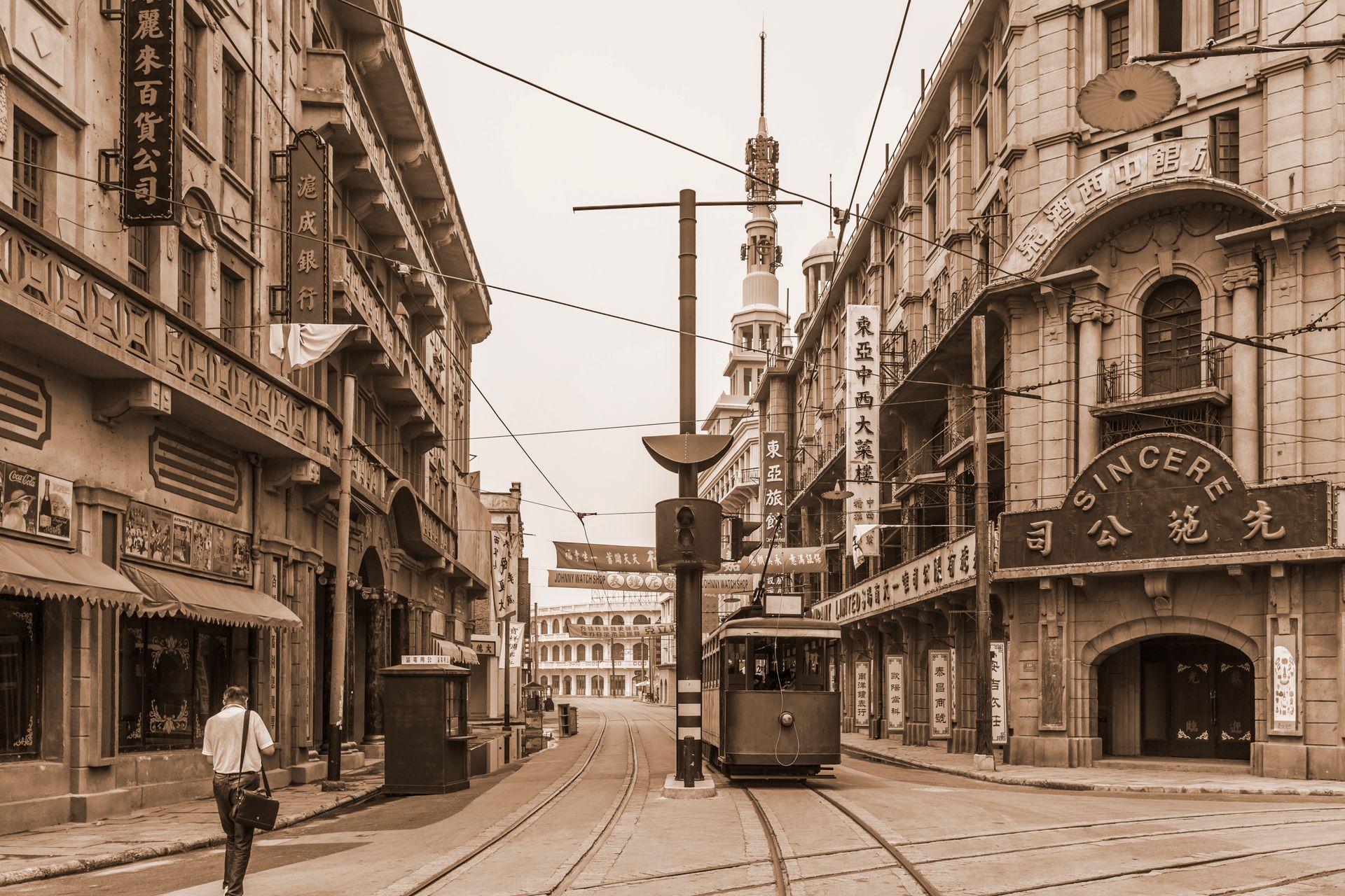 Street scene in sepia tone, Shanghai. A tram travels down tracks. Buildings with signs and awnings line the street.