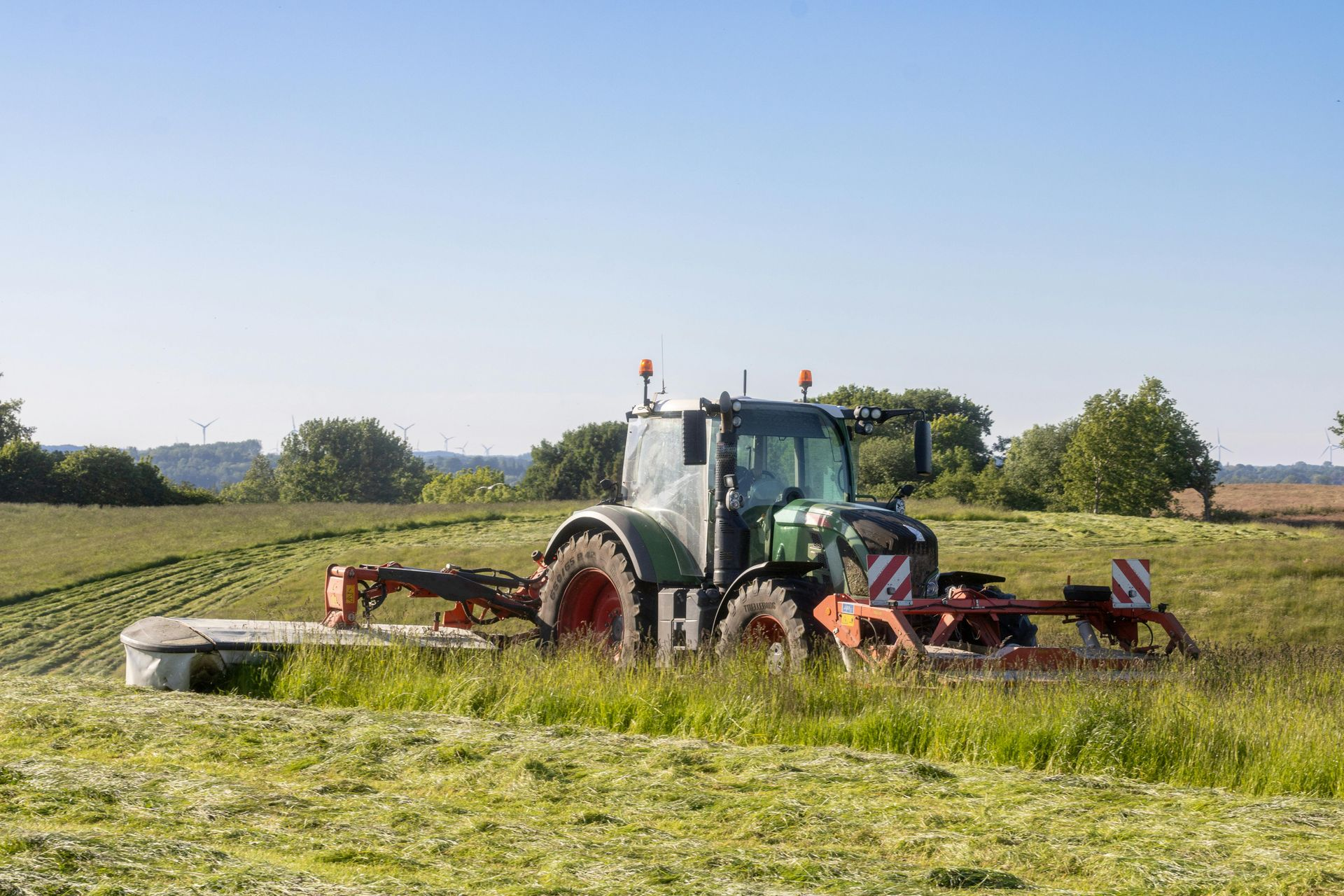 Tractor cutting grass in a field, under a clear blue sky.