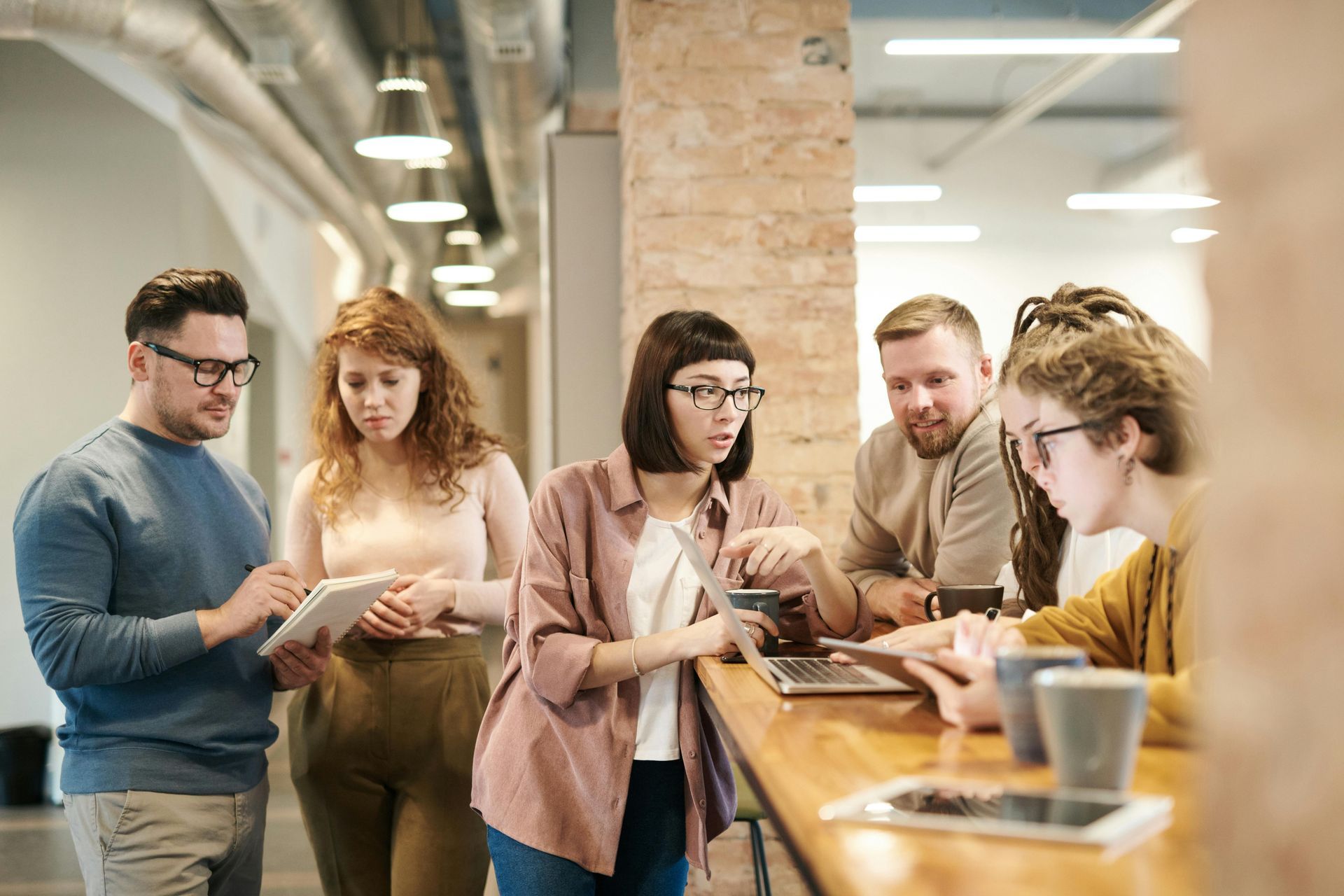 Coworkers collaborating around a laptop in a modern office, pointing and discussing details.