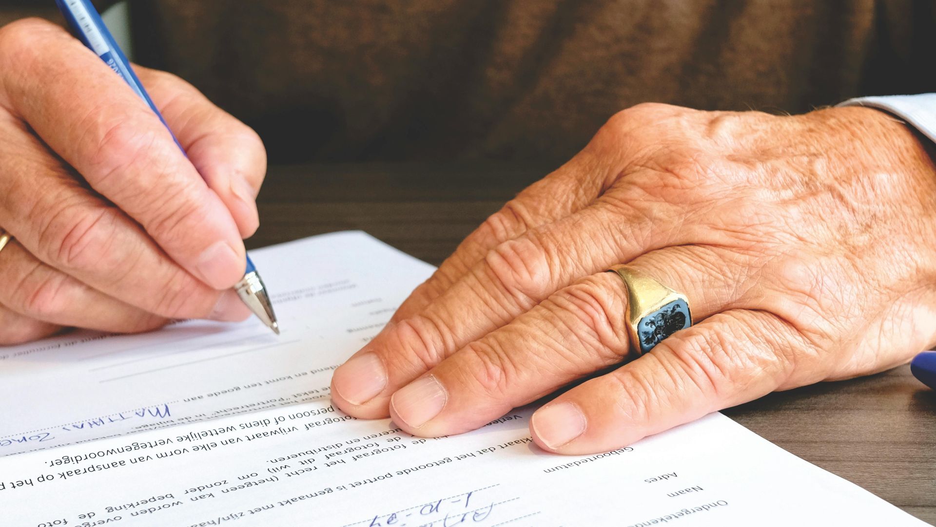 Person's hand with ring holding a pen, writing on paper.