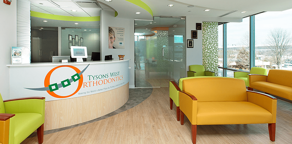 A modern orthodontist's waiting room with lime green and yellow seating. The reception desk has a logo that says