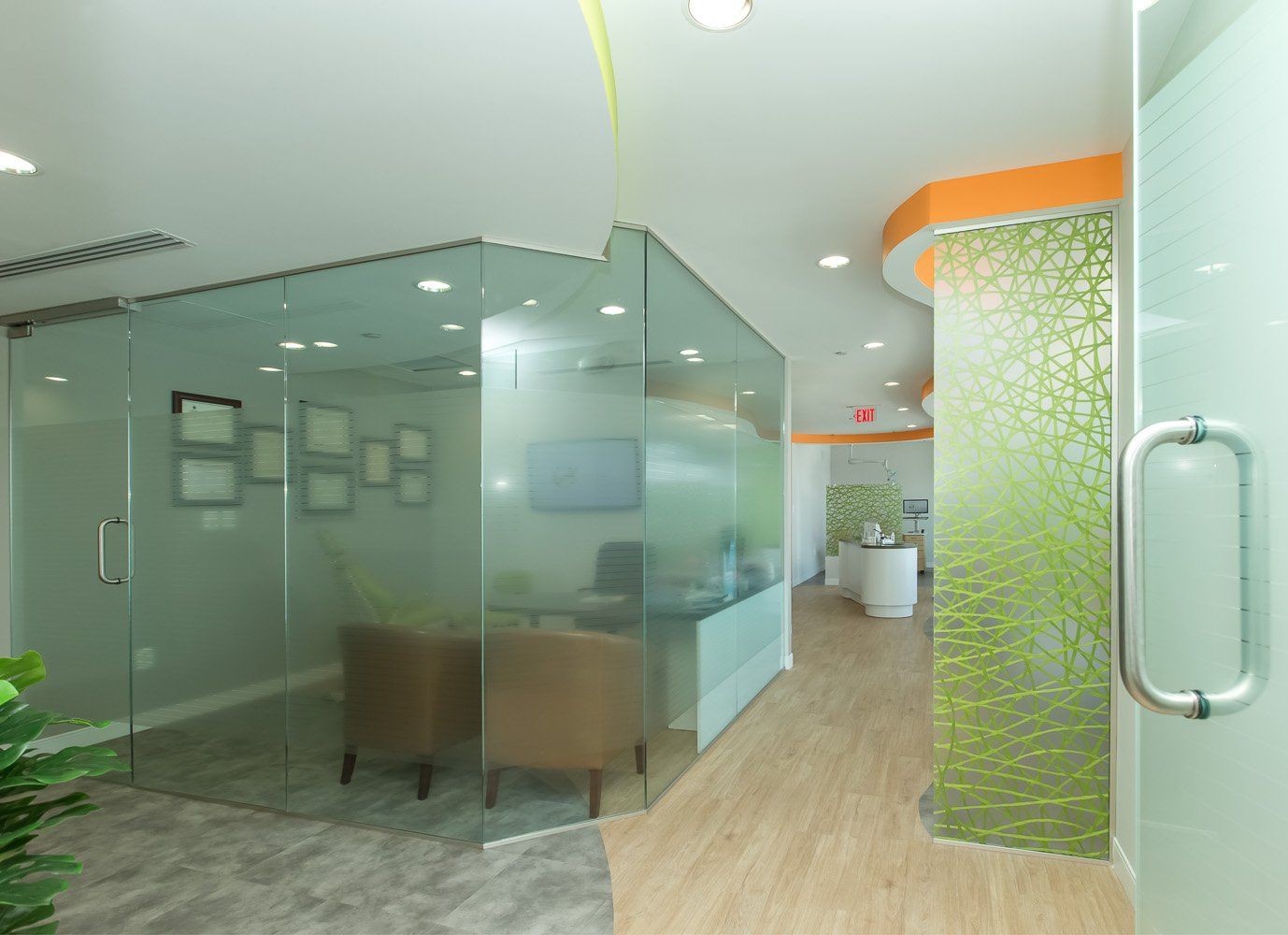 Modern office interior with glass walls, light wood floors, and orange and green accents.