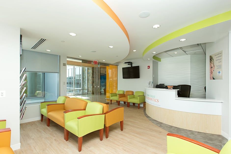 Waiting room: orange/green seating, reception desk, light wood floor, curved ceiling accents.