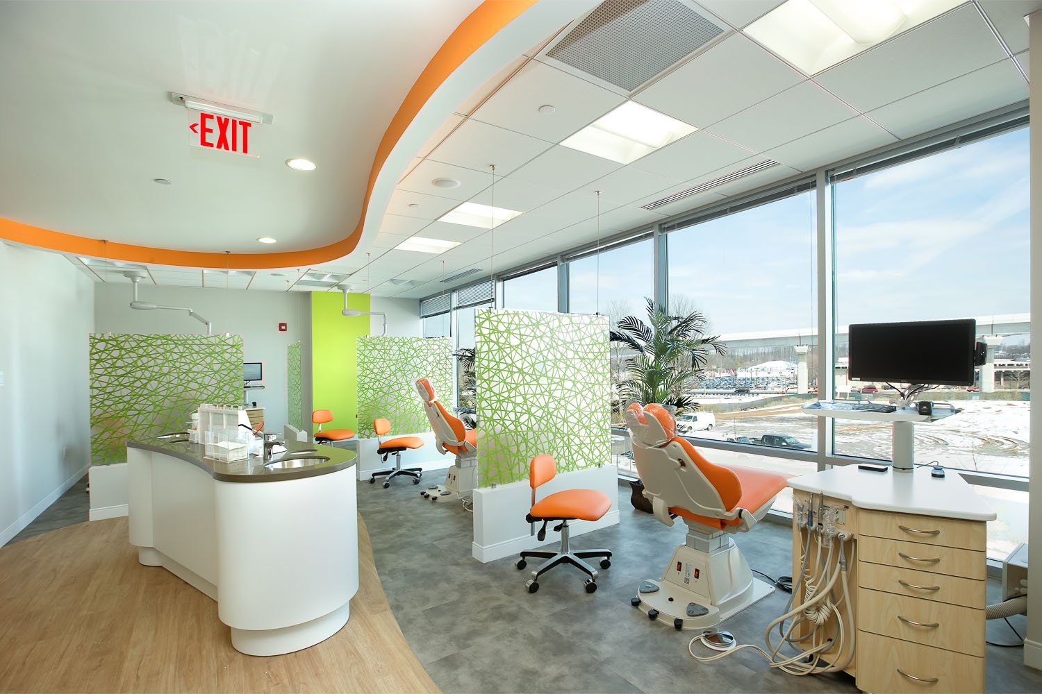 Bright dental office with orange and green accents, large windows, and patient chairs.