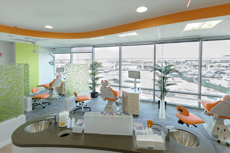 Modern dental office with orange chairs, large windows overlooking a city, and green accents.