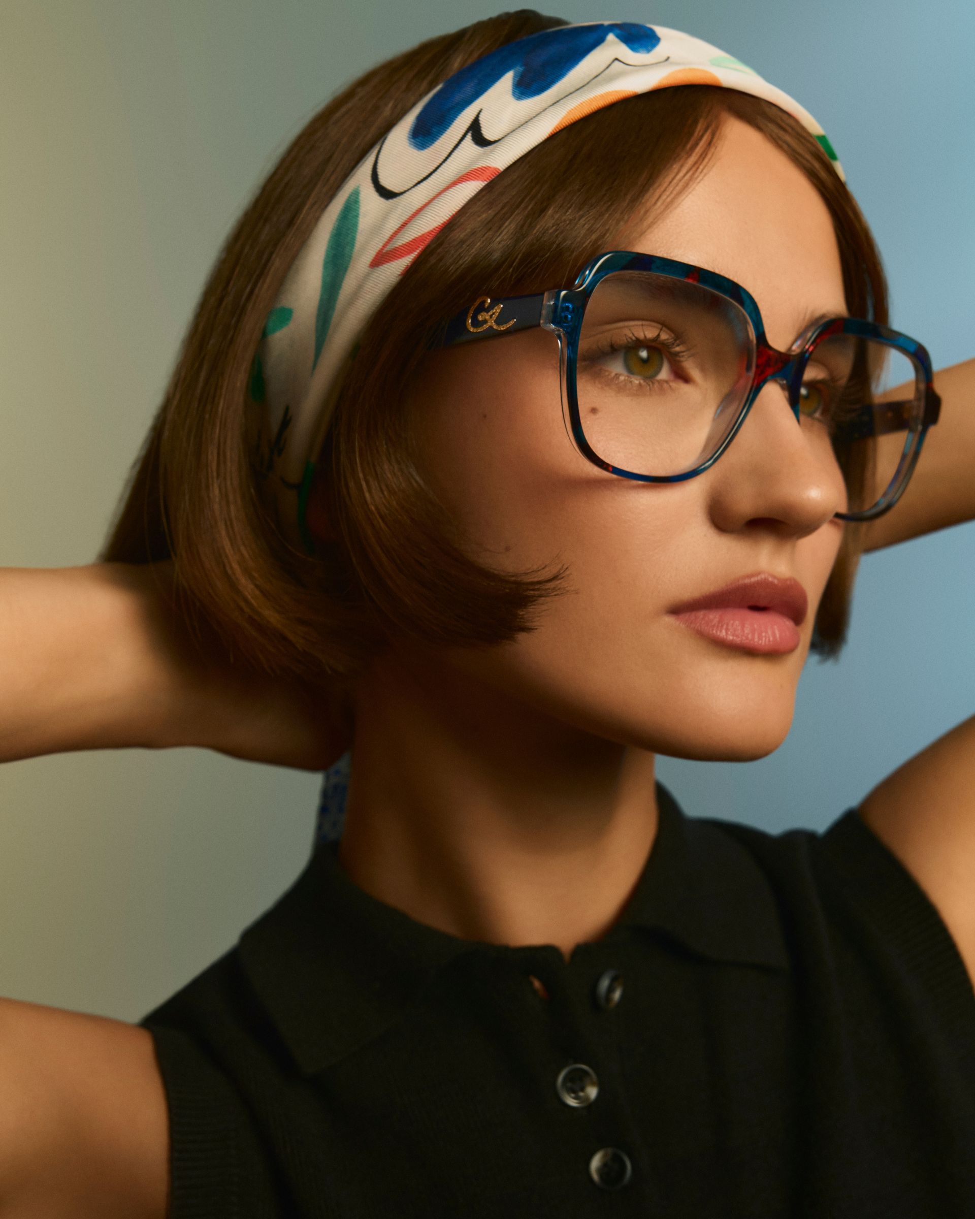 A person smiling and holding a pair of tortoise-shell glasses in front of their face inside an optical shop.