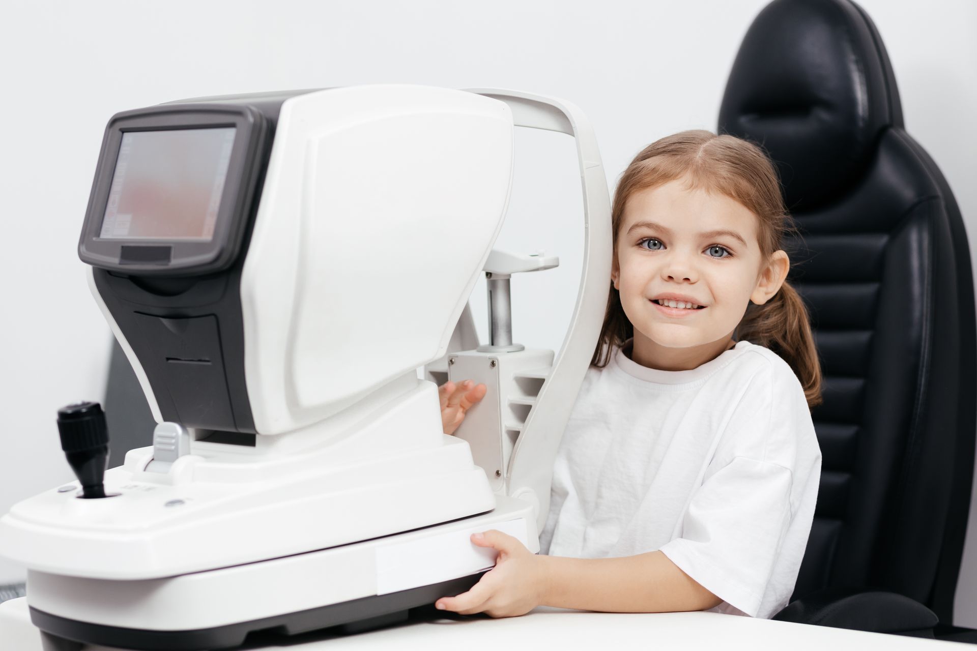 A happy little girl in an ophthalmology clinic next to an ophthalmic instrument.