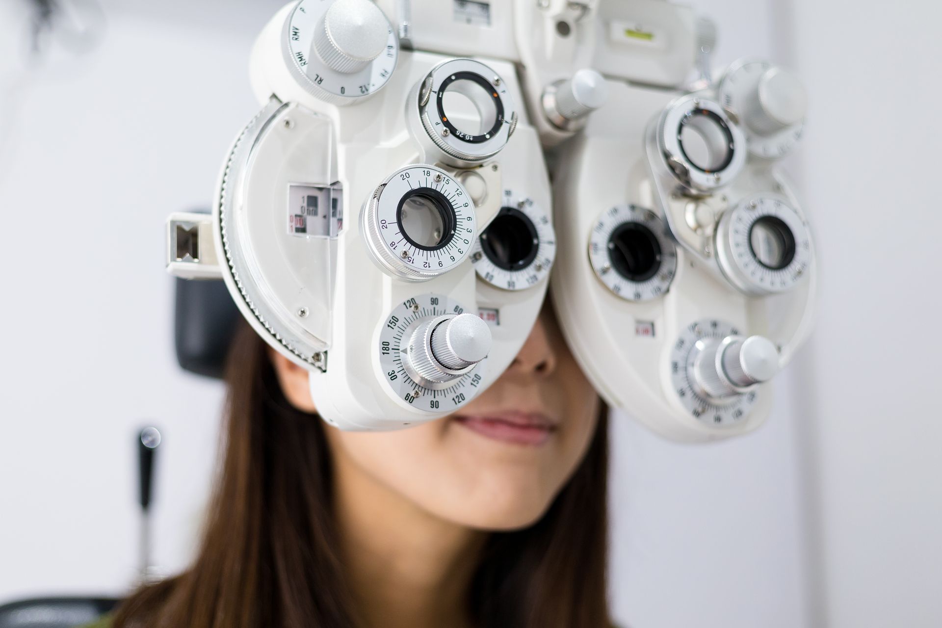 A person undergoing an eye exam, looking through a phoropter in a clinical setting.