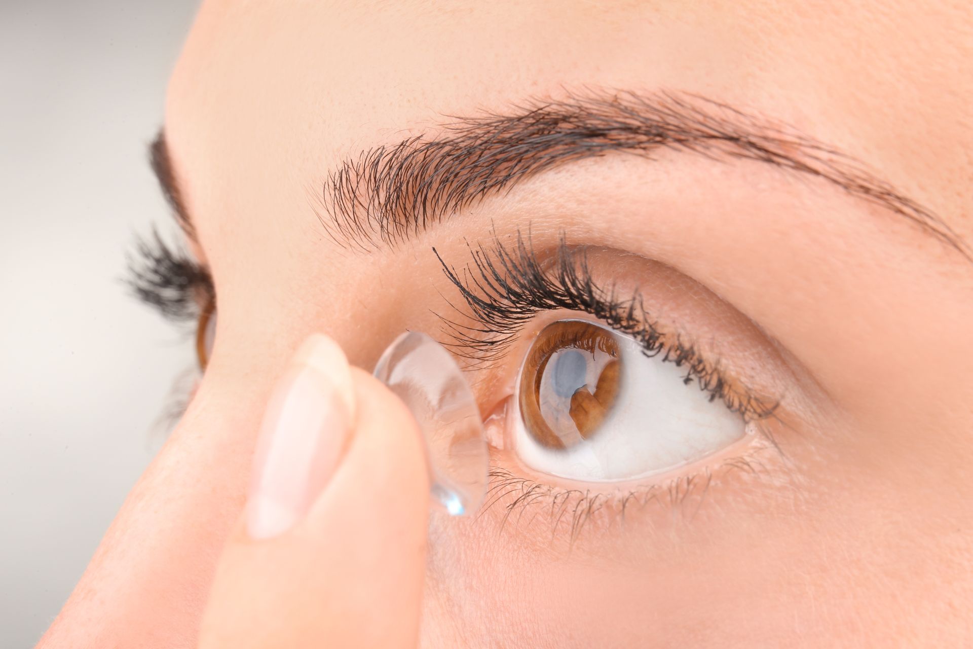 A person holding a clear contact lens near their eye to insert it.