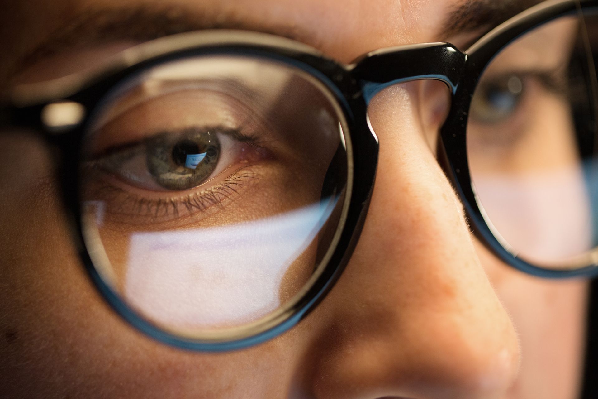 Close-up of a person wearing black-rimmed glasses, with a computer screen reflected in the lenses.
