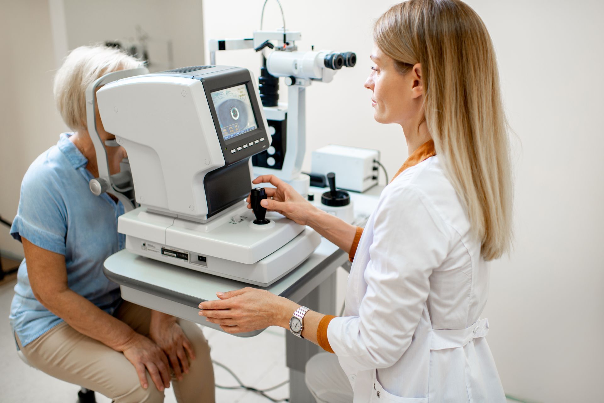 An eye doctor uses a stationary medical device to examine a patient's vision in a bright, modern clinic setting.