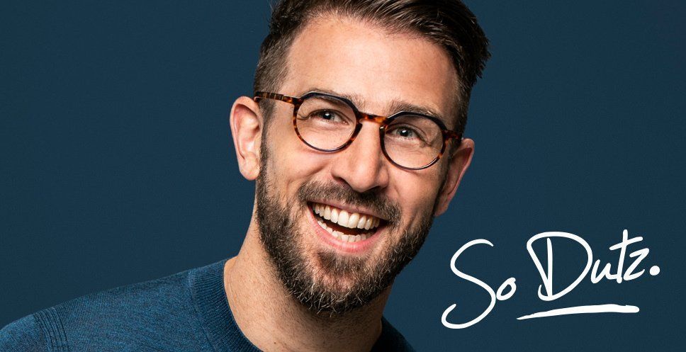 A smiling person with a beard wearing tortoise-shell glasses, set against a dark blue background with the text