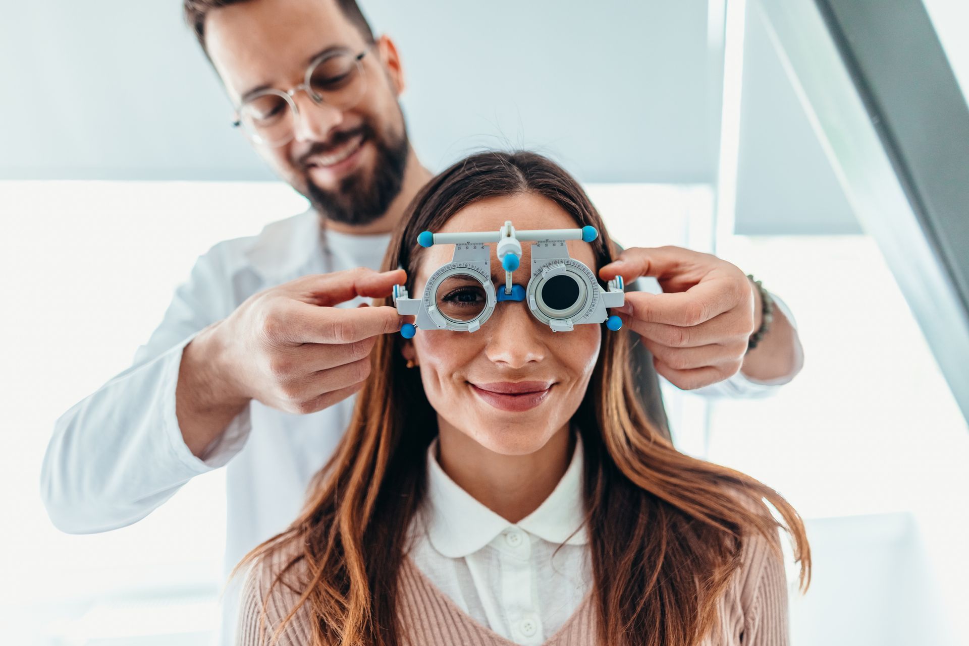 An optometrist performs an eye exam on a patient using a trial frame to test their vision.