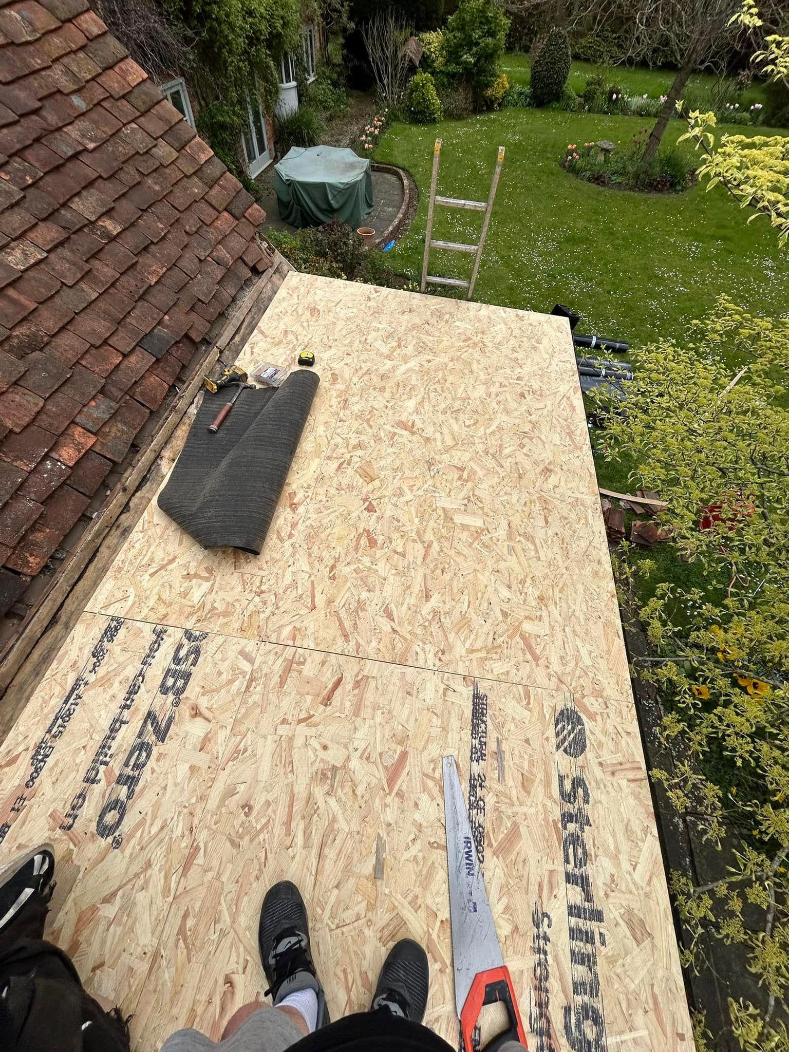 A person is standing on top of a wooden base of a roof with a saw.