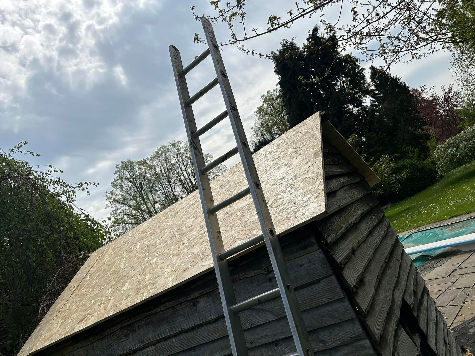A ladder is sitting on the side of a small wooden building with a roof under repair