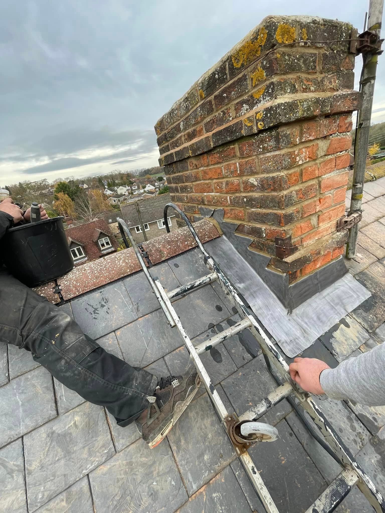 A roofer is working on a slate roof next to a chimney.