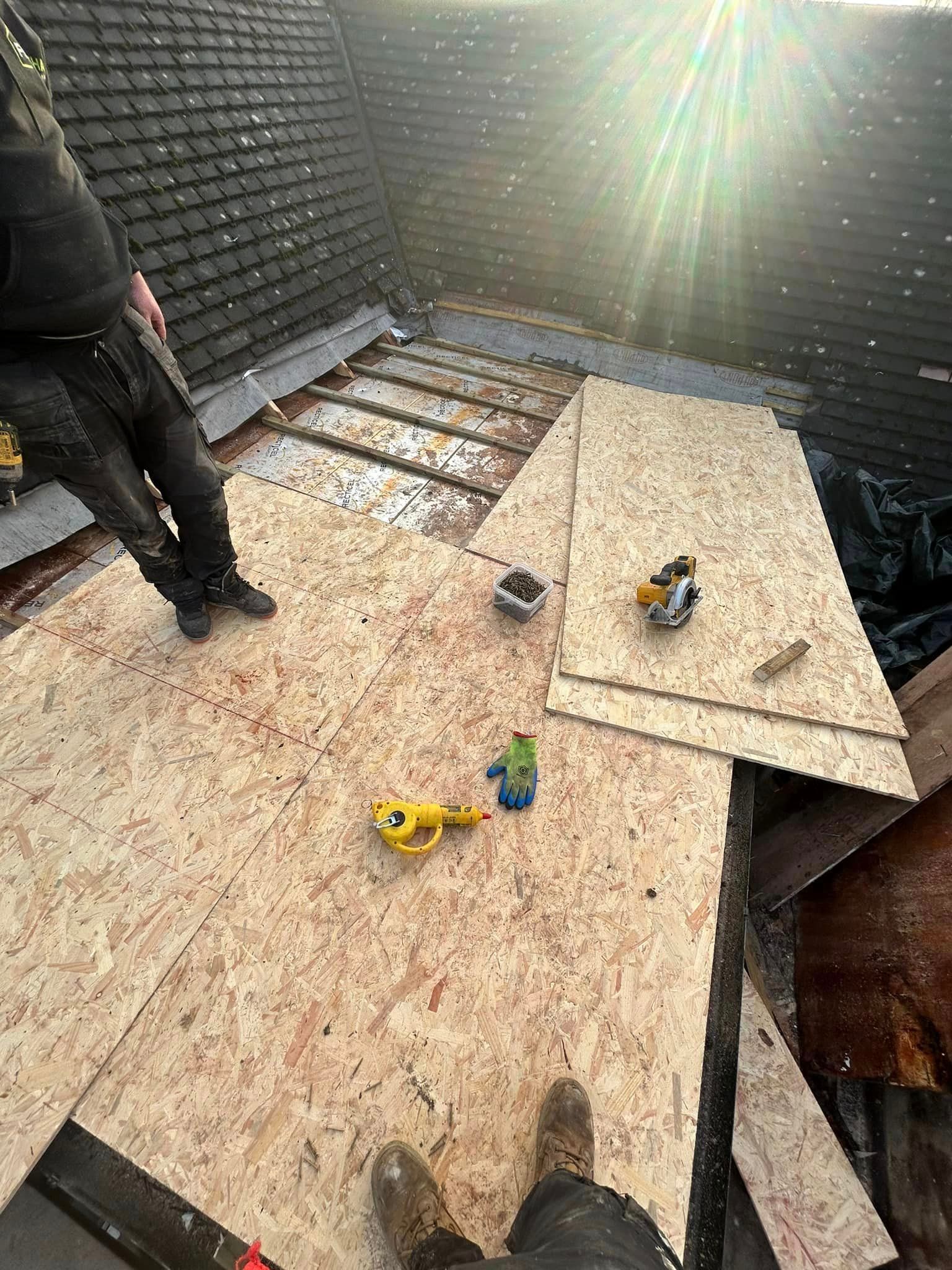 A person is standing on the wooden base of a flat roof being repaired.