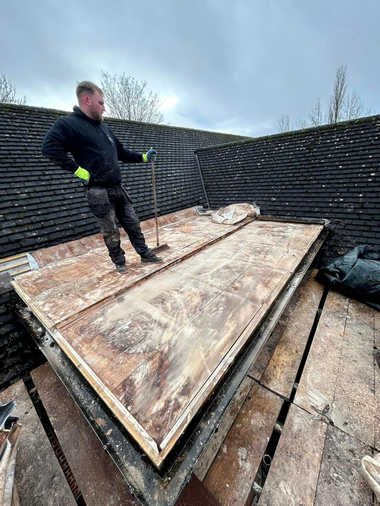 A man is standing on top of a wooden base of a roof under construction.