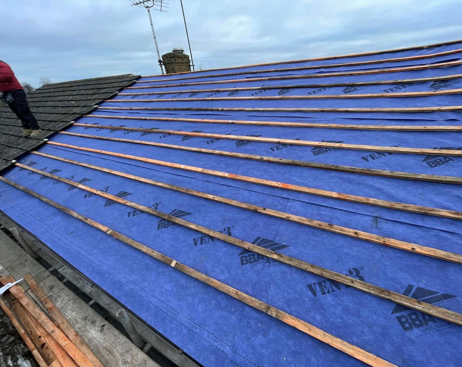 A man is standing on top of a roof with a blue tarp on it.