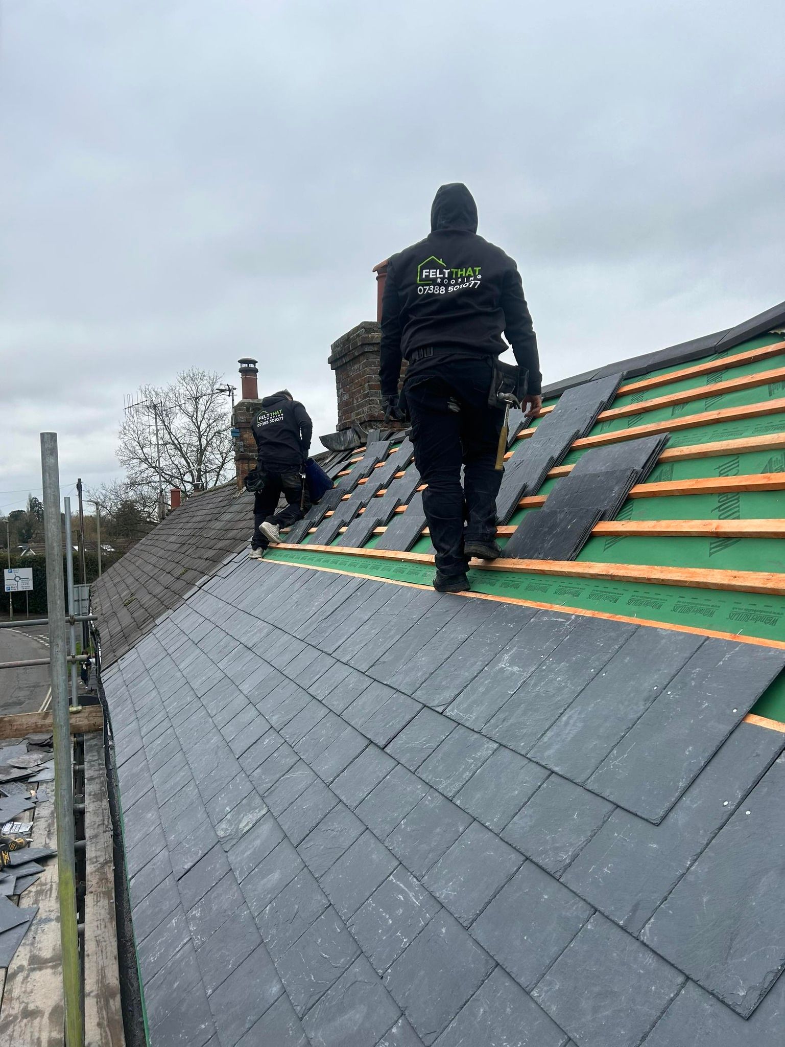 Two roofers are replacing slates on a traditional roof