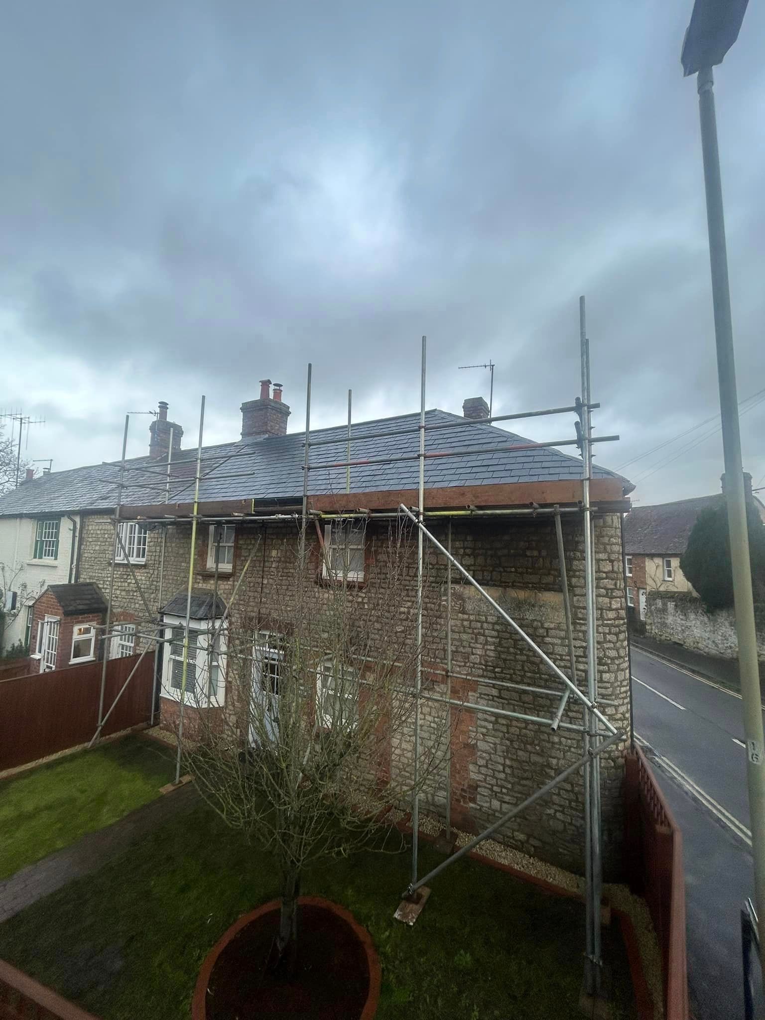 A stone house with scaffolding on the roof and a cloudy sky in the background.