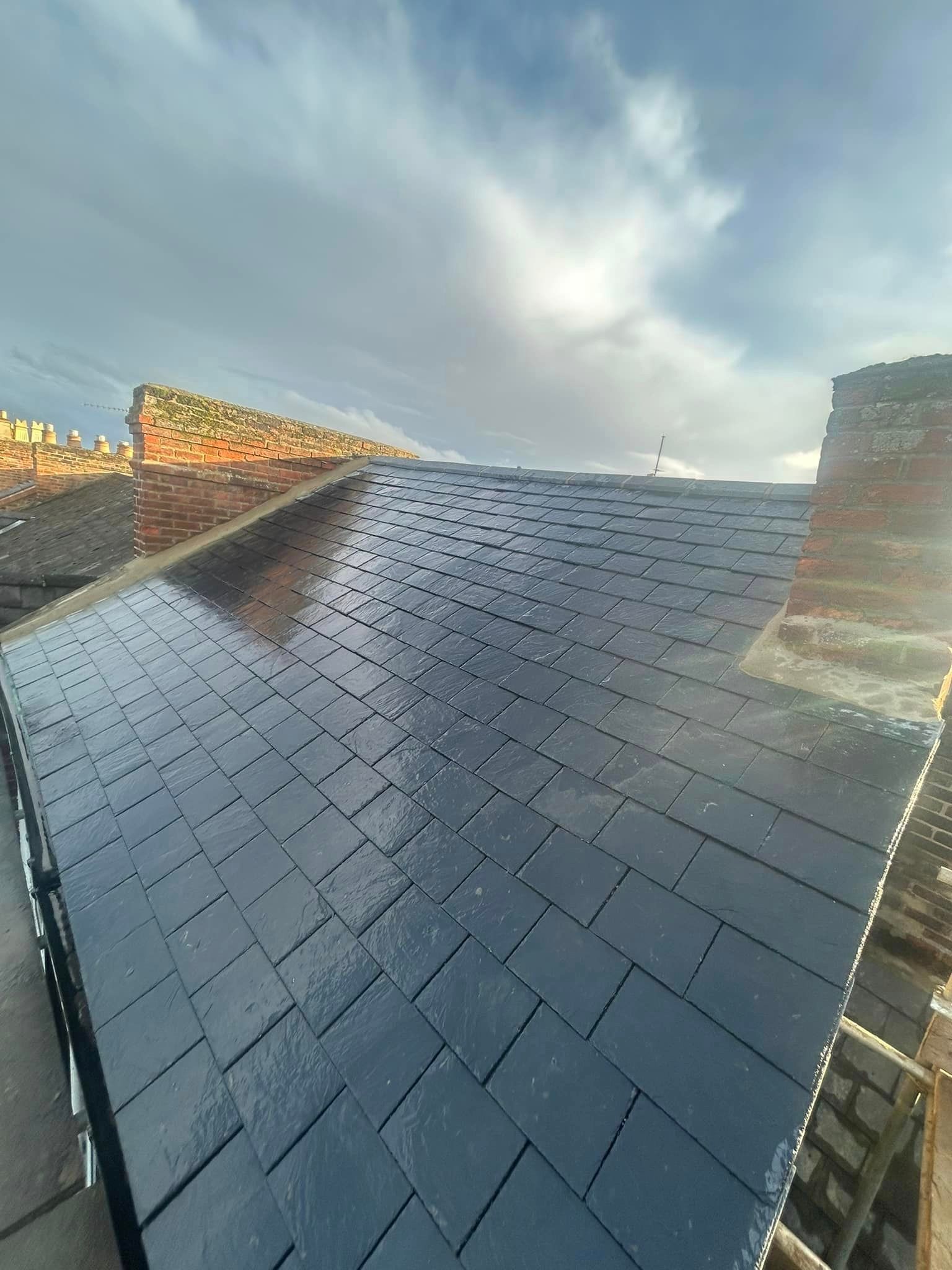 A roof with a lot of black tiles on it and a chimney in the background.