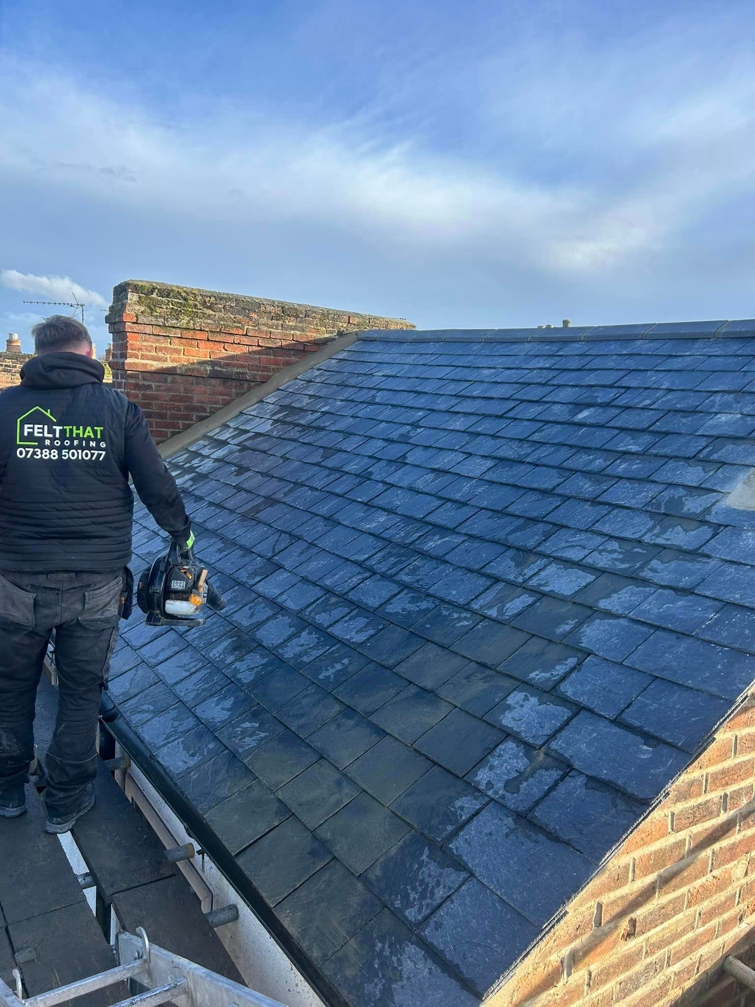 A man is standing on top of a slate roof.