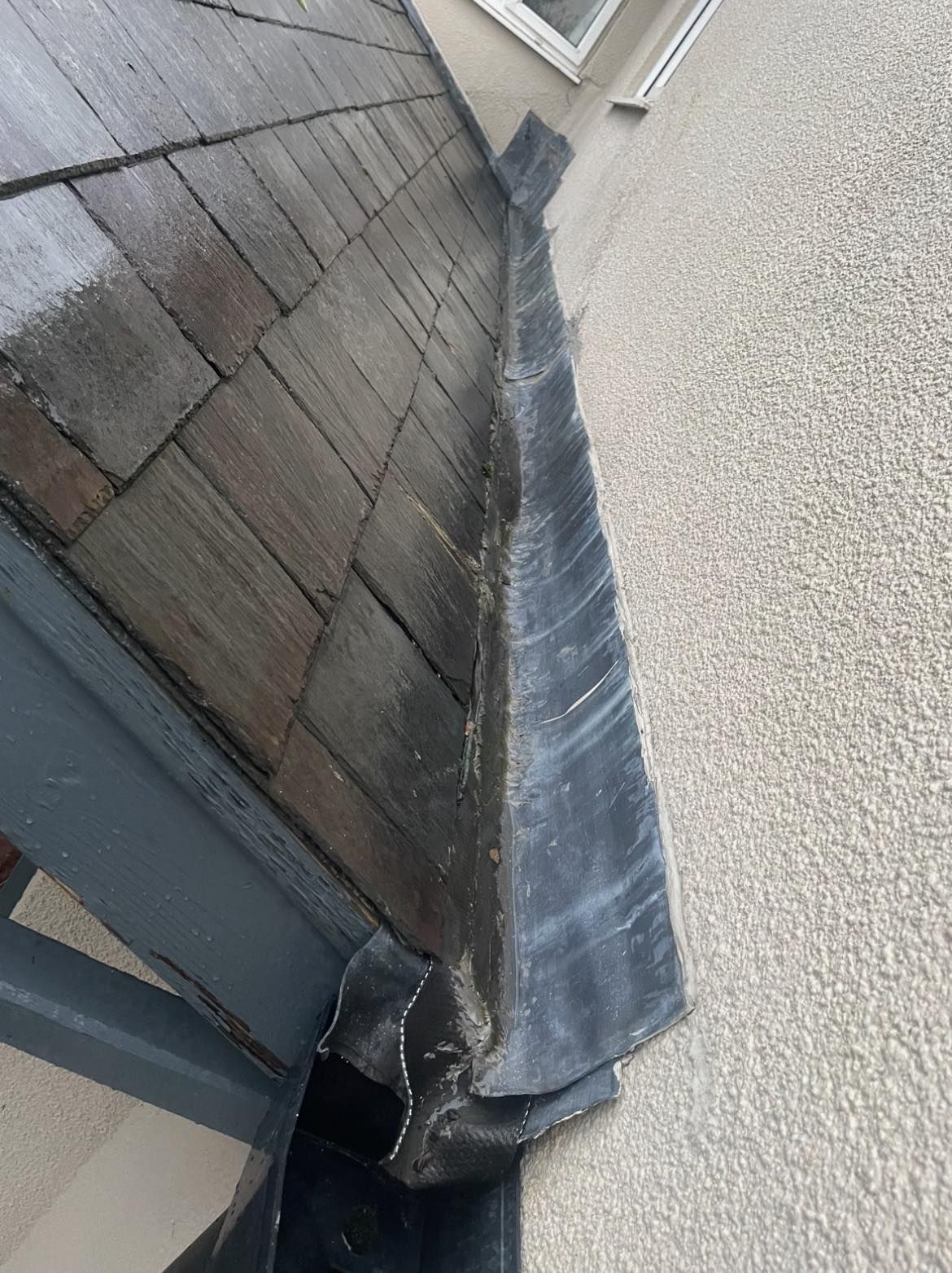 A gutter on the side of a building next to a roof.