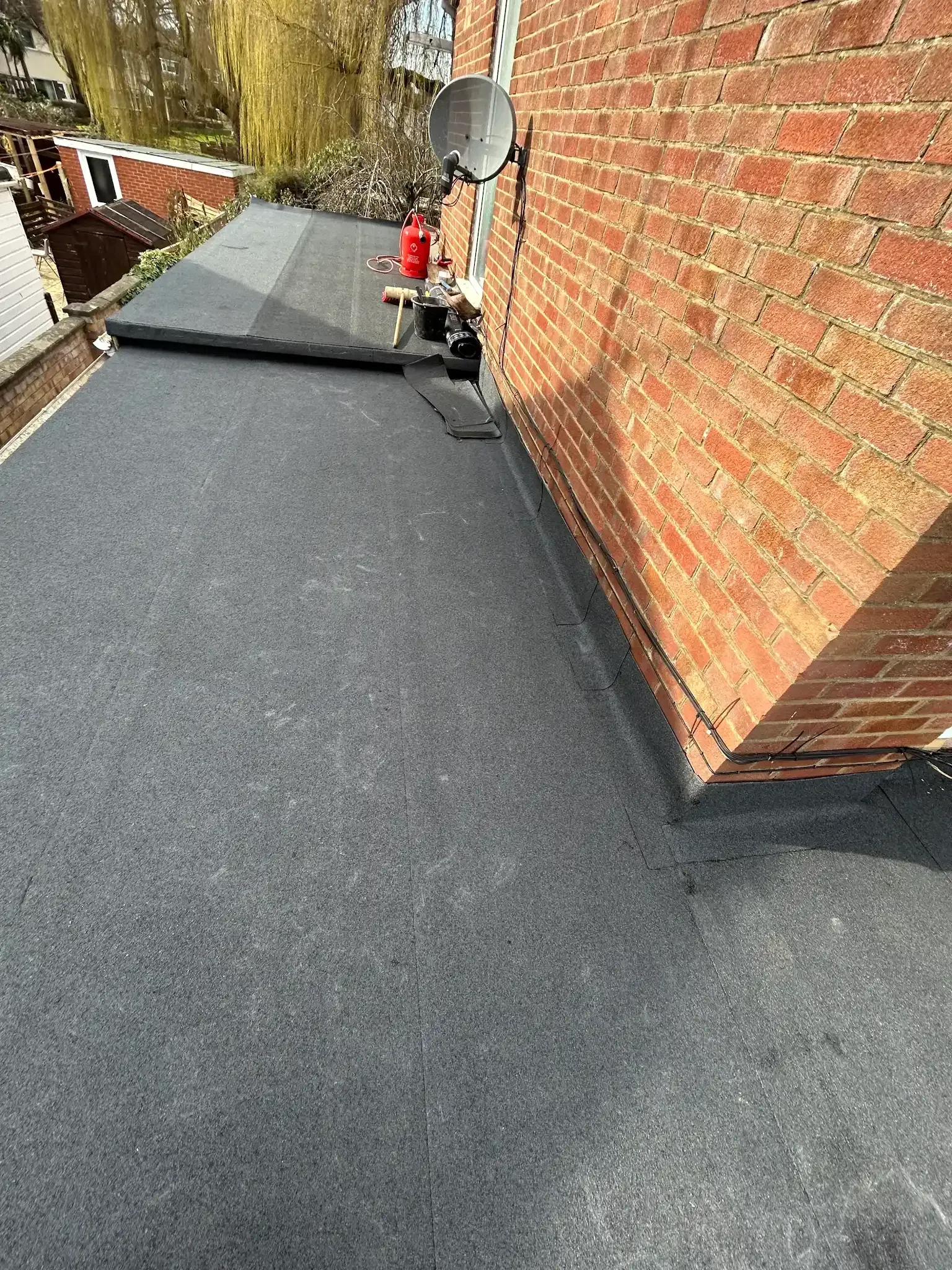 A flat roof is being installed on the side of a brick building.