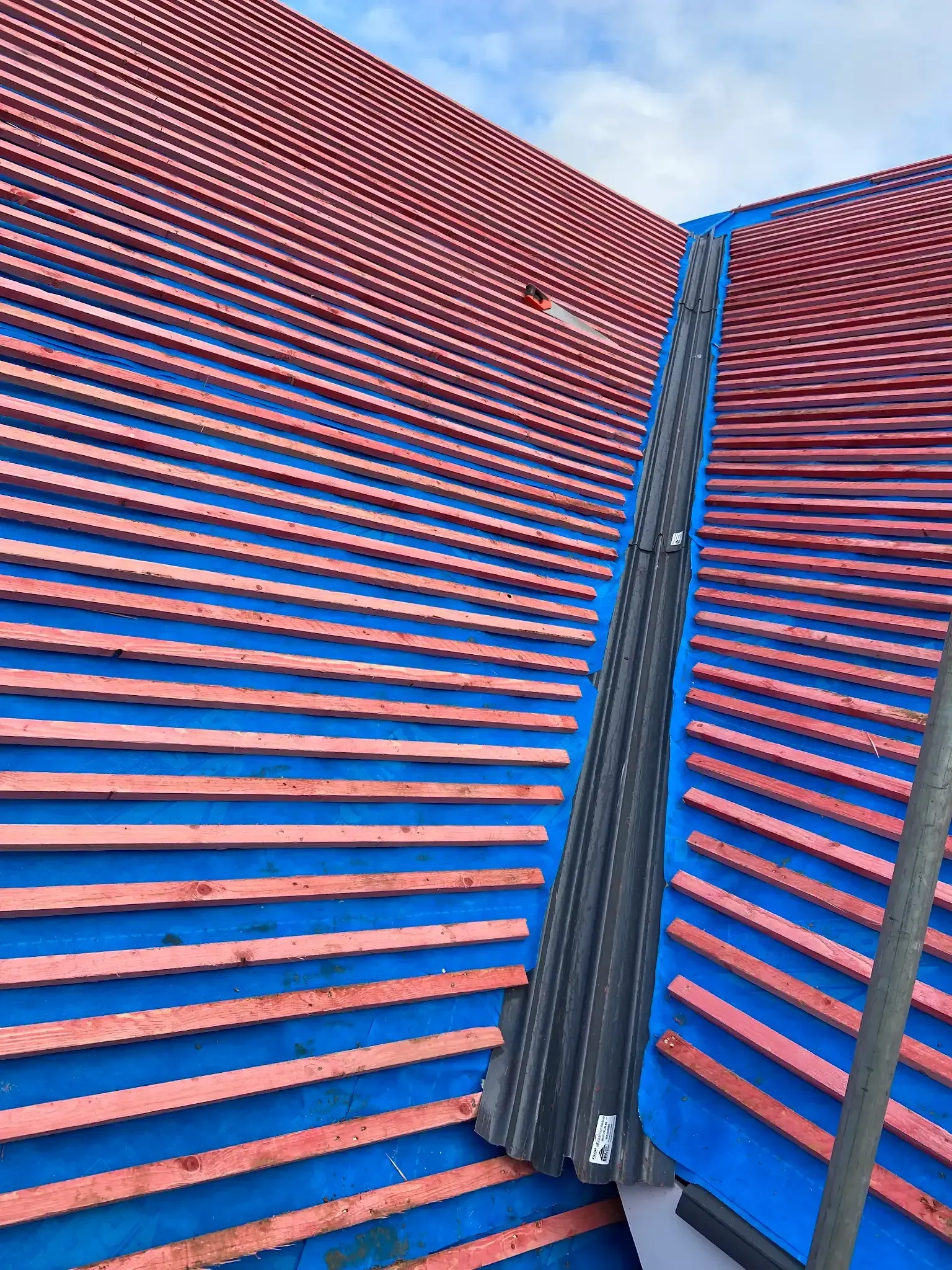 A roof is being built with red tiles and blue shingles.