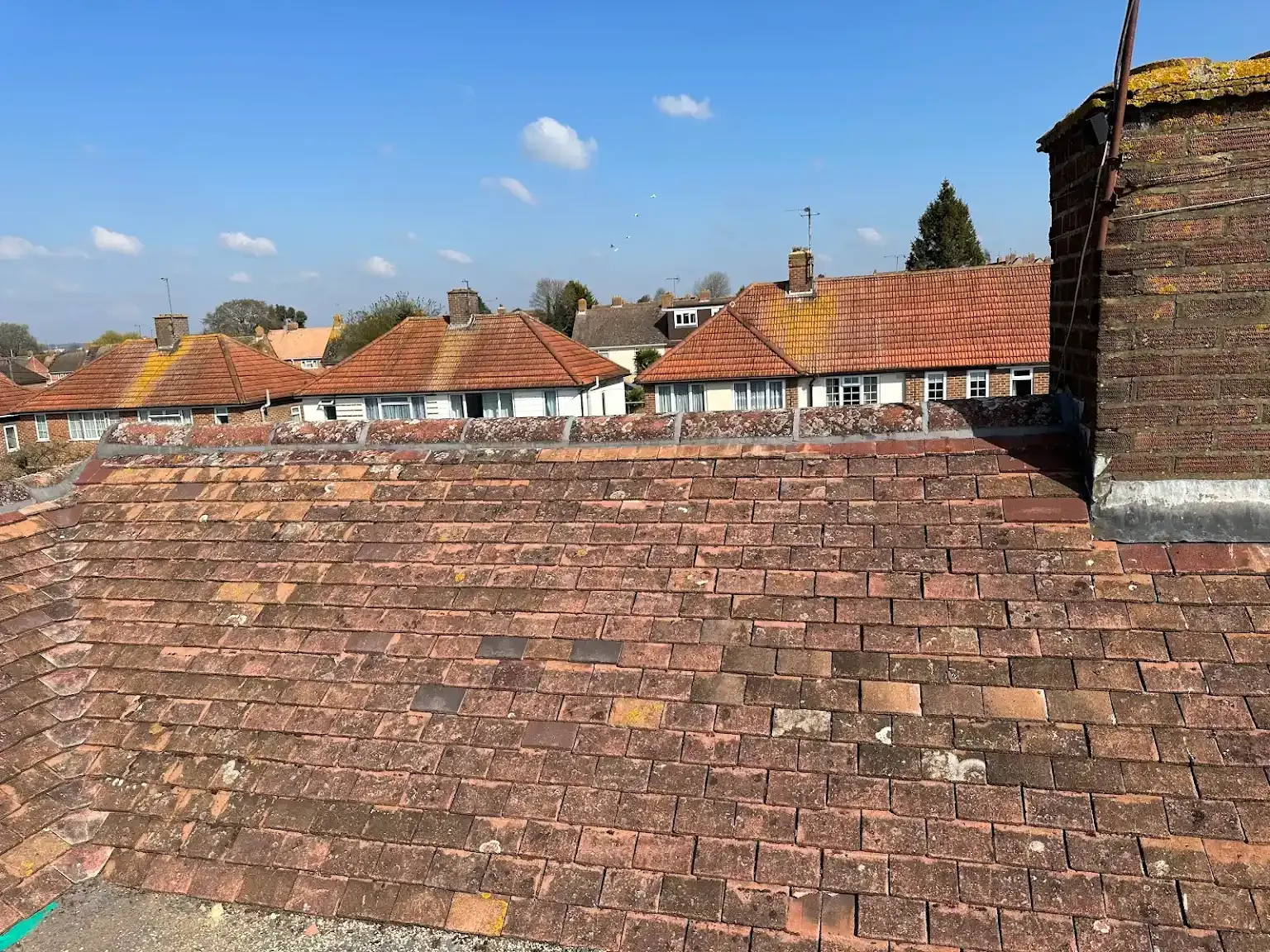 A brick roof with a chimney on top of it and a row of houses in the background.