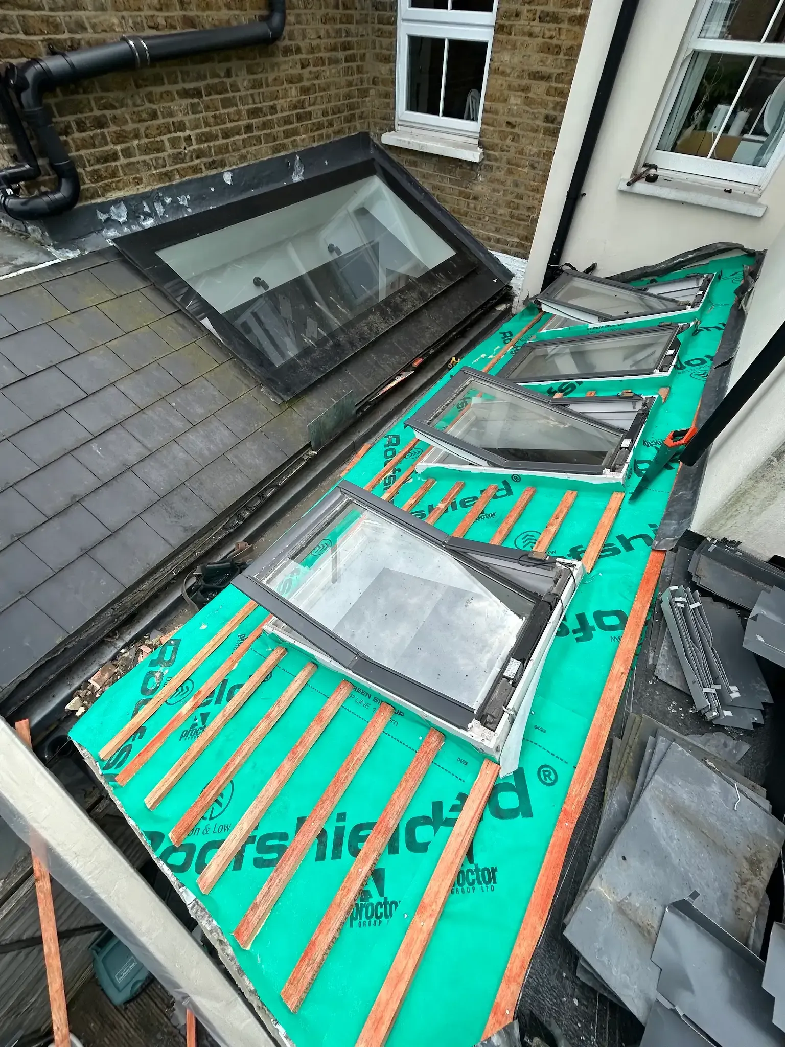 A roof with a green tarp on it and a brick building in the background