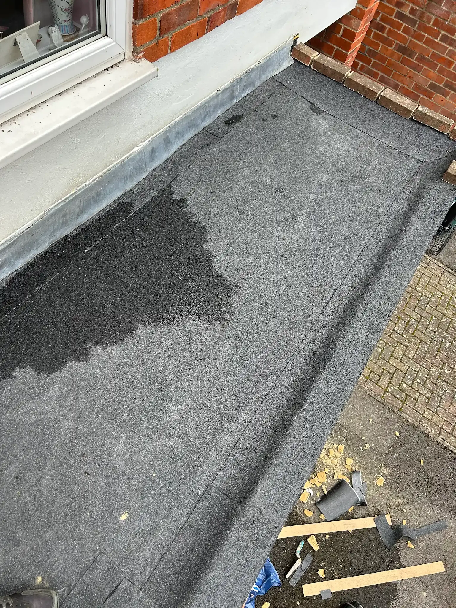 A close up of a flat felt roof with a brick wall in the background.