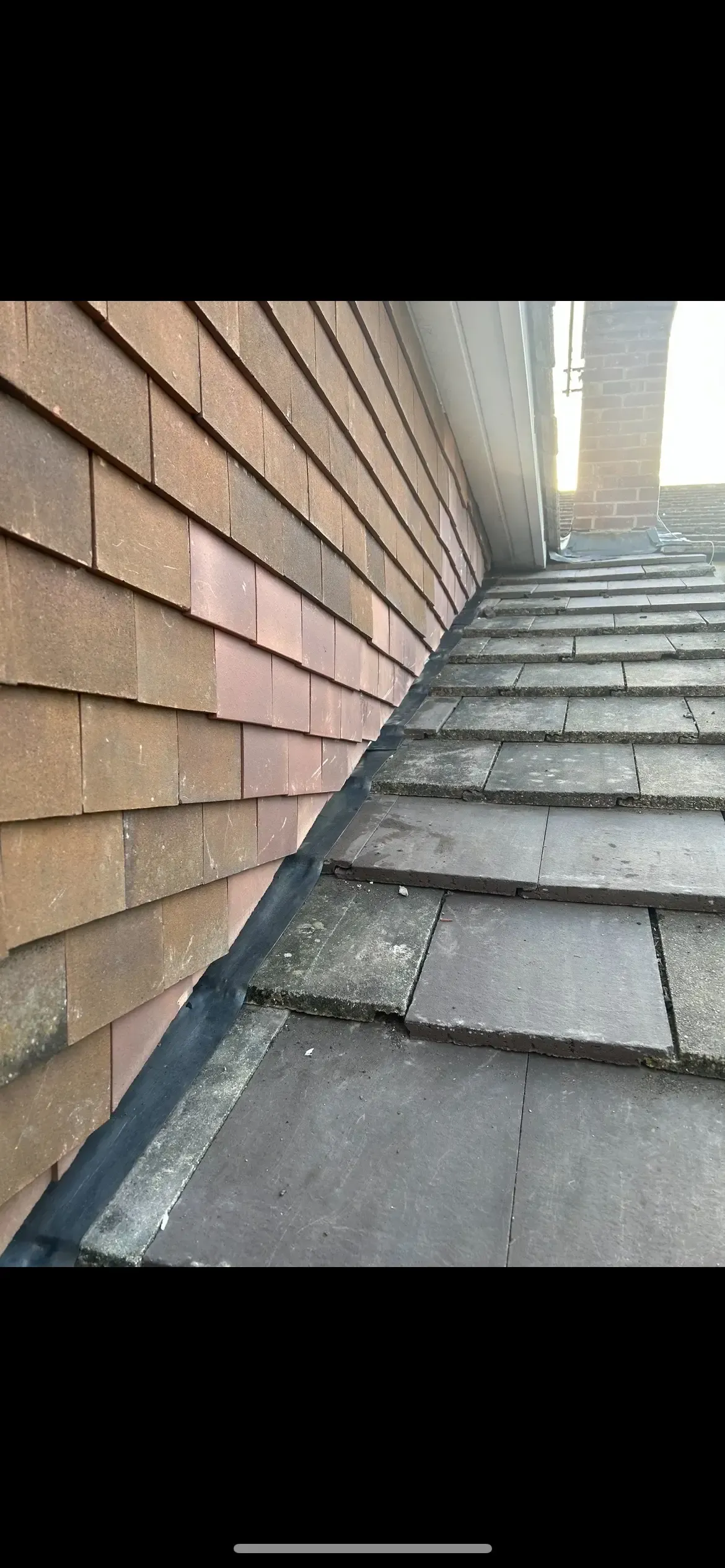 A close up of a roof with a brick wall in the background.