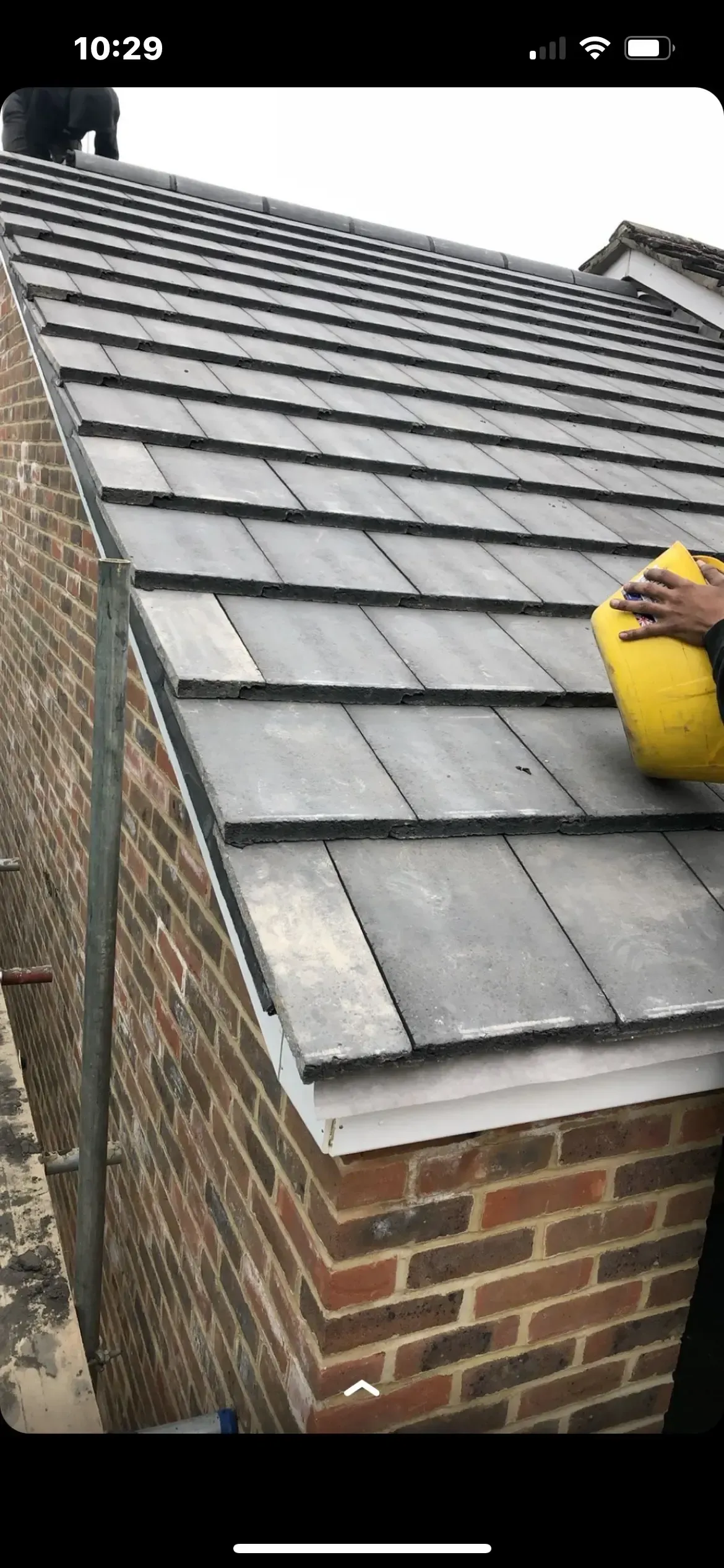 A person is cleaning the roof of a brick building with a yellow bucket.