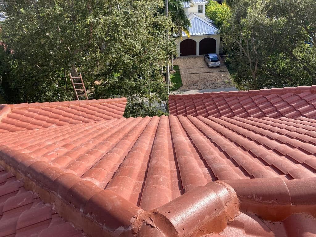 A high-angle view of a red clay tiled roof, with a paved driveway and a garage visible in the background.