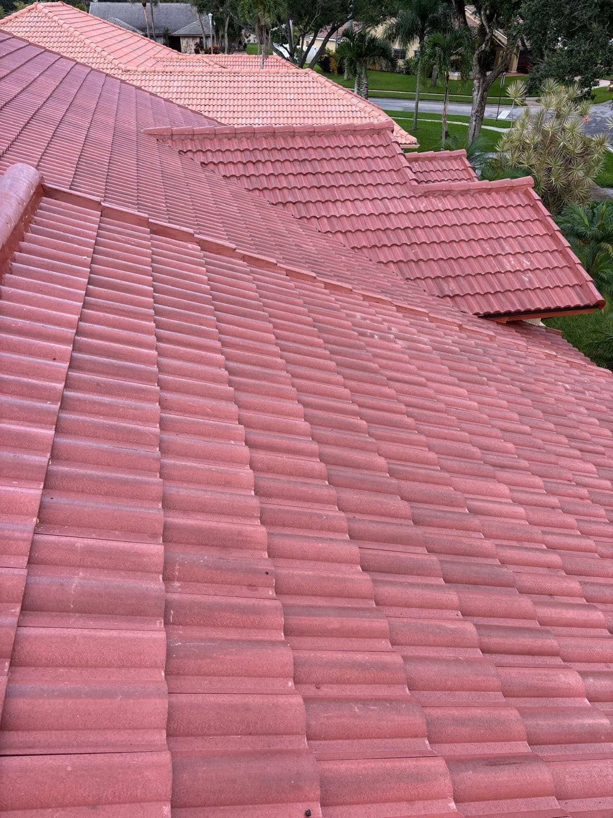 A high-angle view of a residential roof covered in textured, reddish-brown clay tiles.