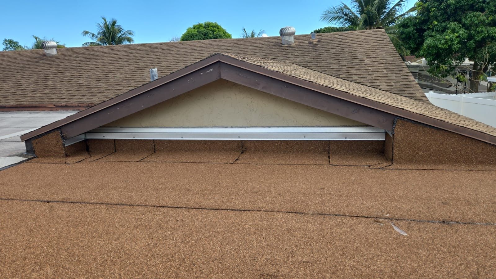 A gravel-covered flat roof features a triangular, brown-trimmed gable section with a horizontal white vent.