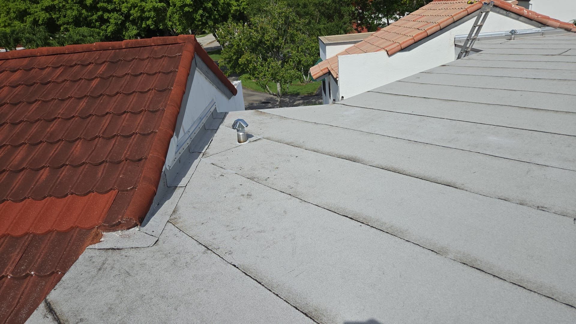 A view of a roof with grey metal panels meeting a red tiled section, with a small metal anchor point installed.