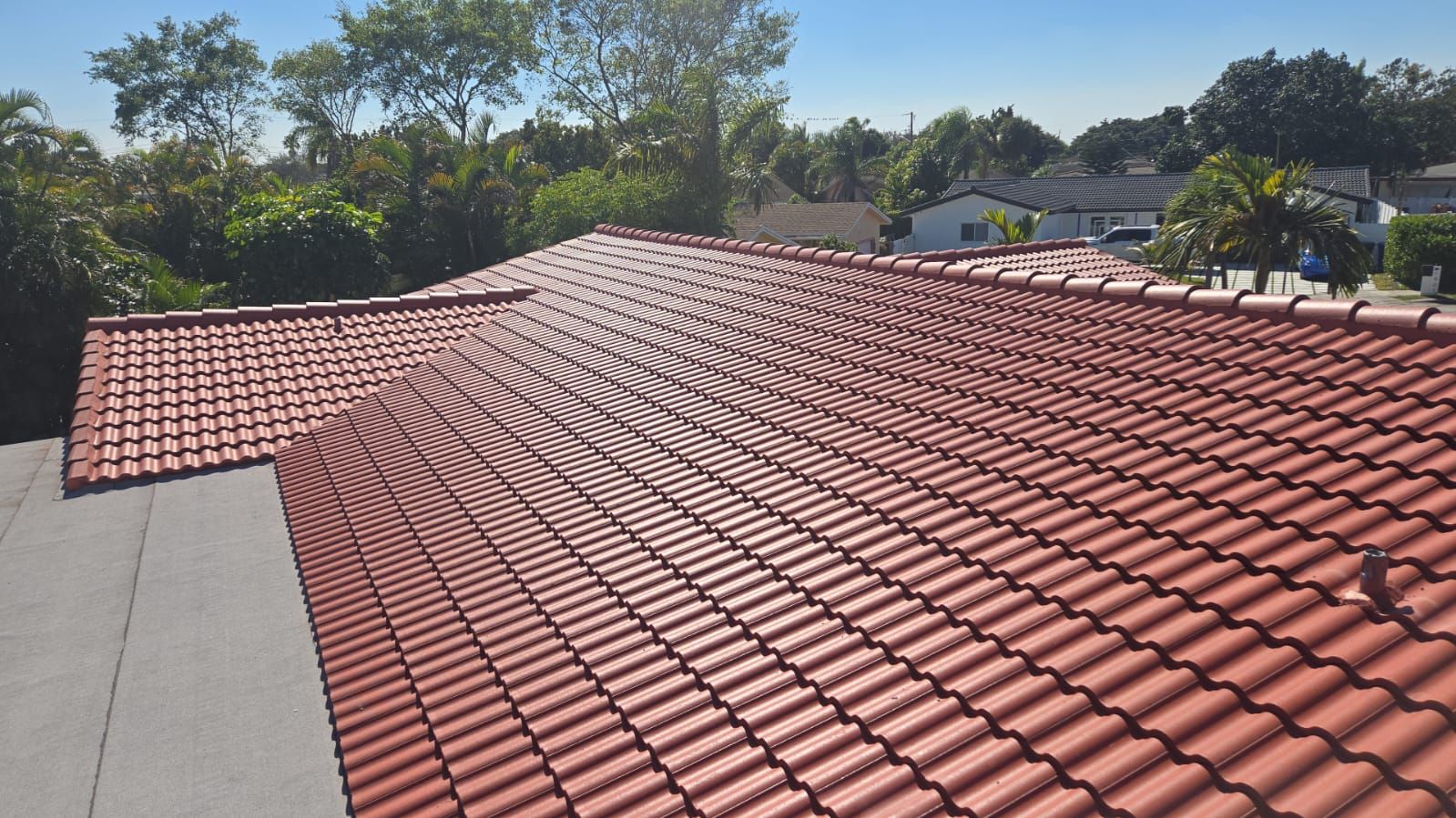 An overhead view of a roof with red barrel tiles, featuring a valley where two slopes meet and a section of grey underlay.
