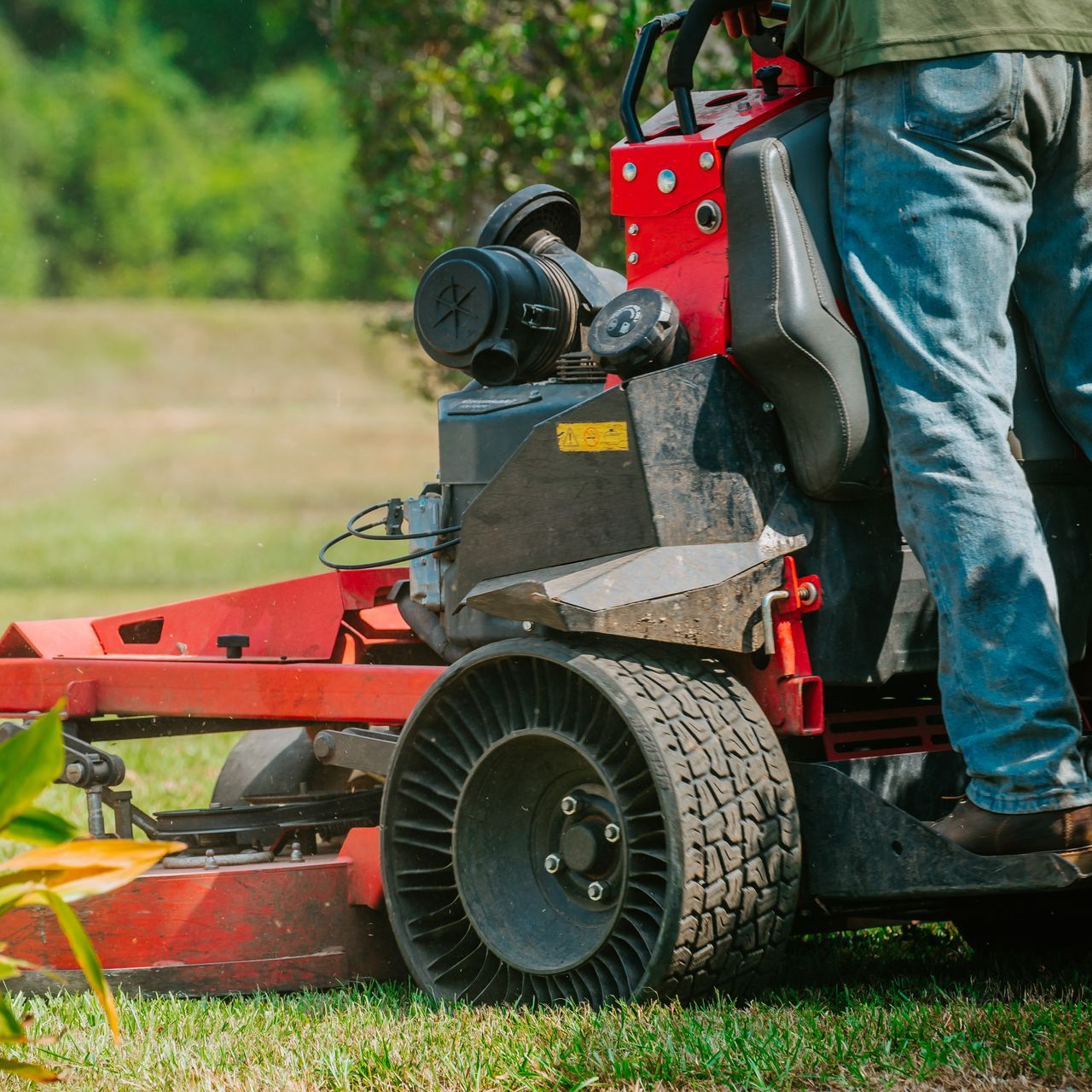 Red lawn mower on grass, with a person standing beside it.
