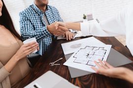 People shaking hands over a floor plan on a desk during a real estate meeting