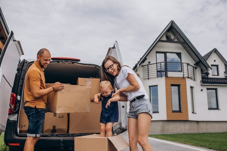 Family loading moving boxes into a car outside a suburban house