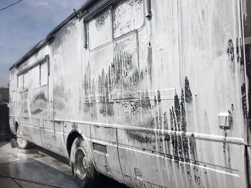 A dirty bus is covered in foam and is being washed.